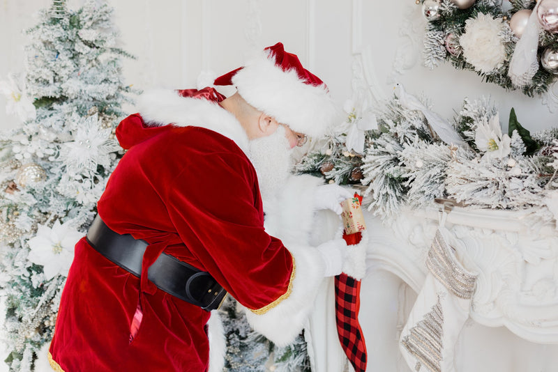 Person in a Santa Claus costume standing next to a decorated Christmas tree.